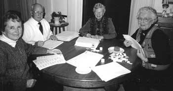 Four members of the mailing crew seated around a table covered with envelopes