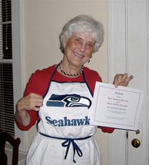 Barb Bowman in a Seahawks apron, holding up a certificate